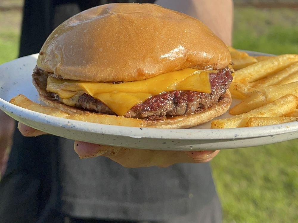 Plato con hamburguesa con cheddar y papas fritas servido al aire libre